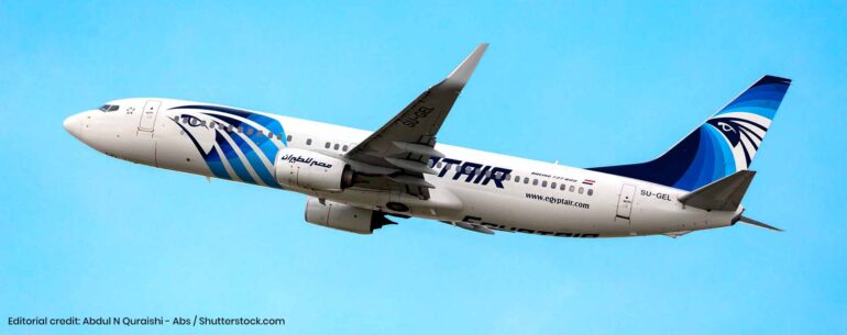 EgyptAir passenger jet in blue and white livery flying against a clear blue sky.